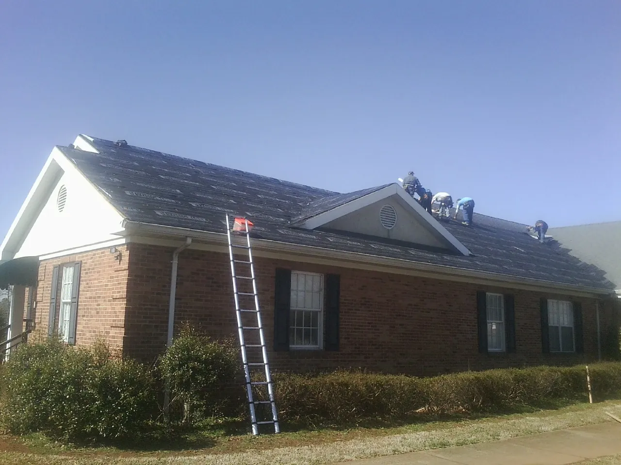 Crew tearing shingles off a brick ranch roof with a ladder set — Metal Roof Repair work by our crew in Woodside
