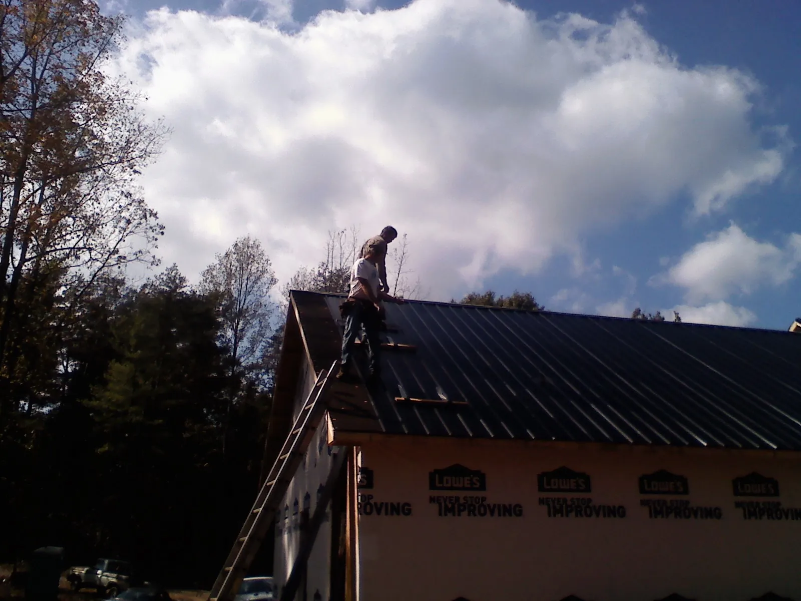 Roofer fastening dark metal panels high against a cloudy sky, from a Roof Inspection job in Woodside